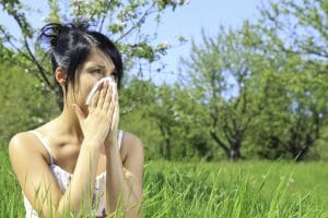 Woman standing in a field blowing her nose. Grass allergy.