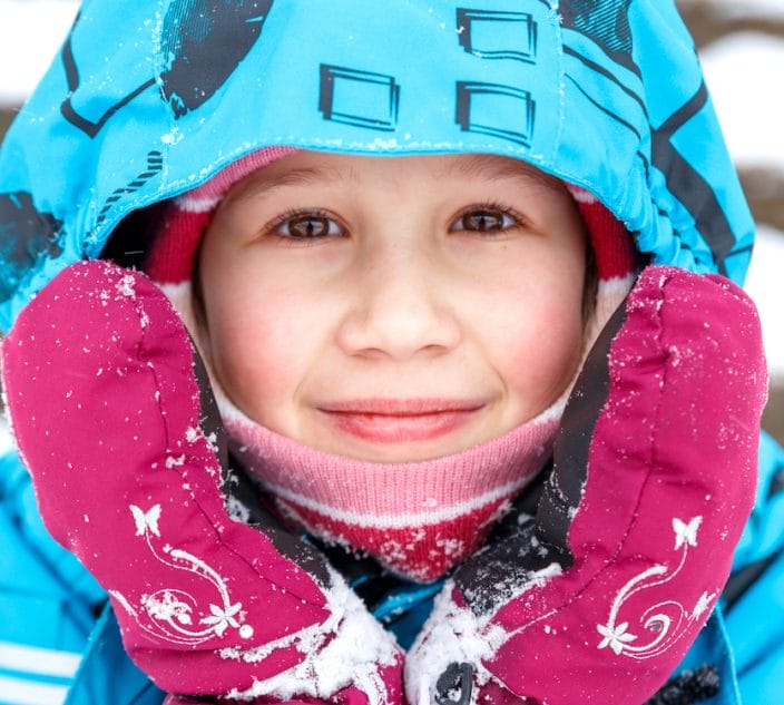 Close-up portrait of bundled up child in the snow.