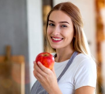 Young woman holding an apple and smiling. oral allergy syndrome