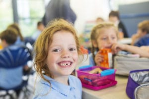 Smiling girl sitting in a school cafeteria. food allergy cafeteria