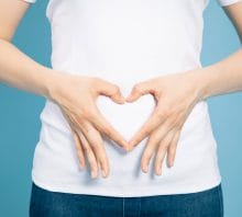 Woman with hands in the shape of a heart over stomach.