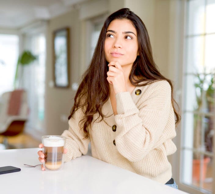 Young woman drinking a cup of coffee at home serious face thinking about question, very confused idea