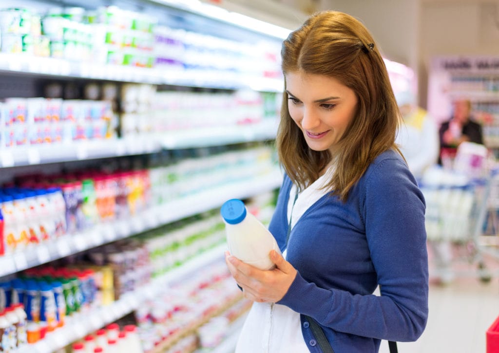 Young woman checking milk's labeling in supermarket.