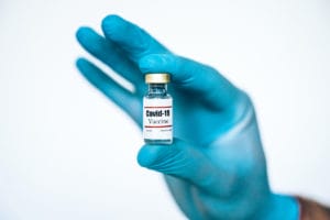 Hand in protective glove holds Coronavirus Covid-19 Vaccine glass bottle.
