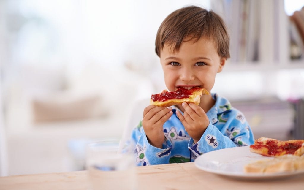 A little boy eating toast with peanut butter and jam