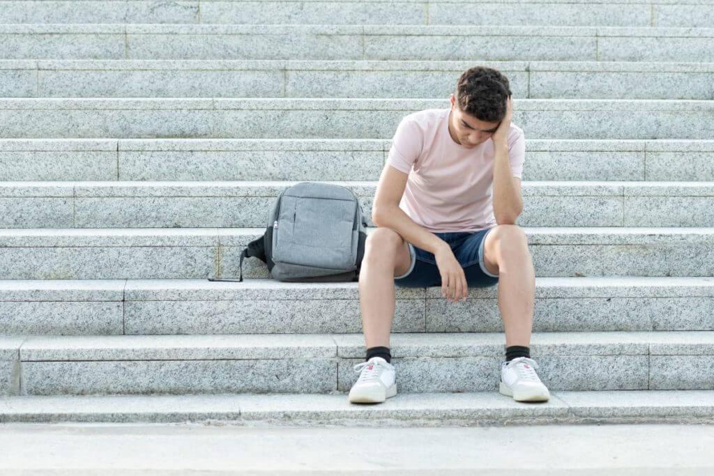 Upset student sitting on steps with his backpack.