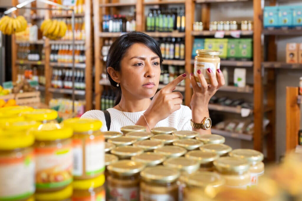 Woman reading product contents on jar while shopping in food department of supermarket