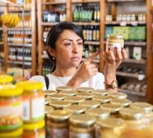 Woman reading product ingredients on jar while shopping.