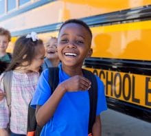 As they wait in line by the school bus, elementary age students goof off and laugh together.