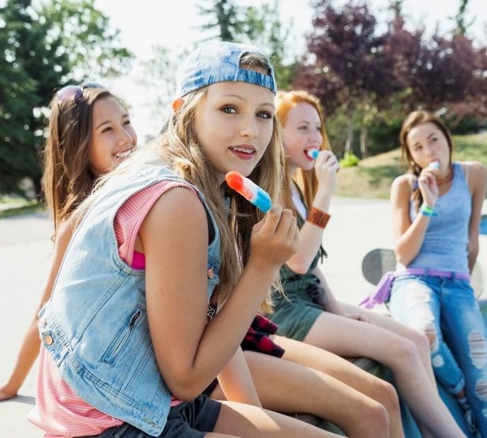 Teenage girls eating flavored ice at skateboard park